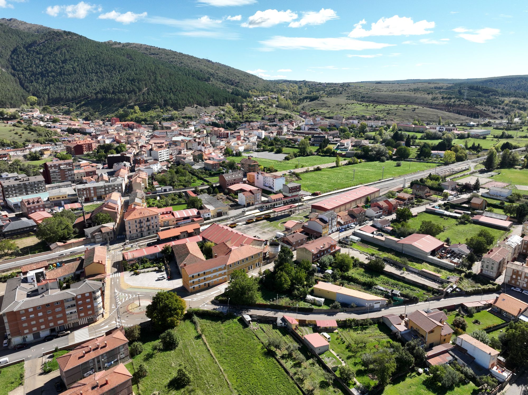 Cistierna y su recinto ferroviario en diagonal, con estación, naves, casas, campos y montaña.
