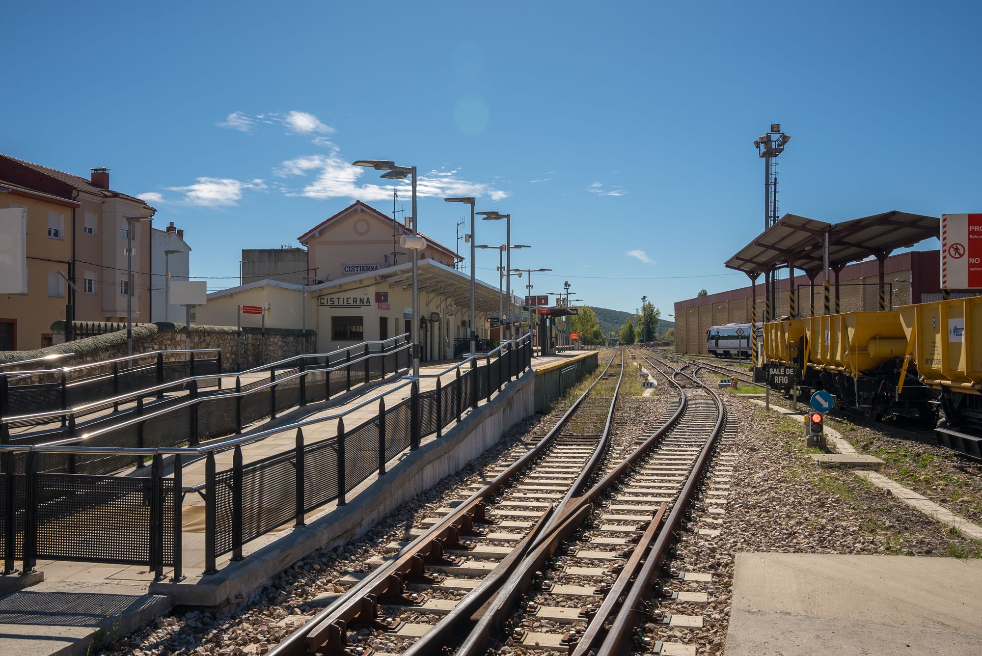 Estación de Cistierna y su andén a la izquierda, desvíos y vagones amarillos a la derecha.